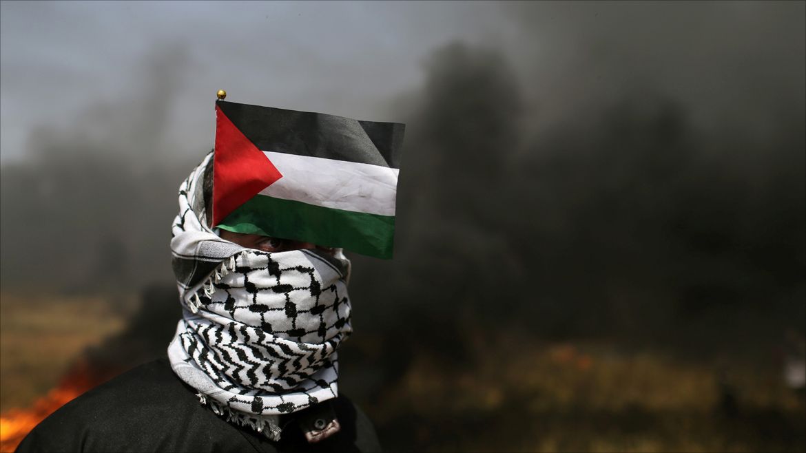 A demonstrator with a Palestinian flag looks on during clashes with Israeli troops at the Israel-Gaza border at a protest demanding the right to return to their homeland, in the southern Gaza Strip April 6, 2018. REUTERS/Ibraheem Abu Mustafa