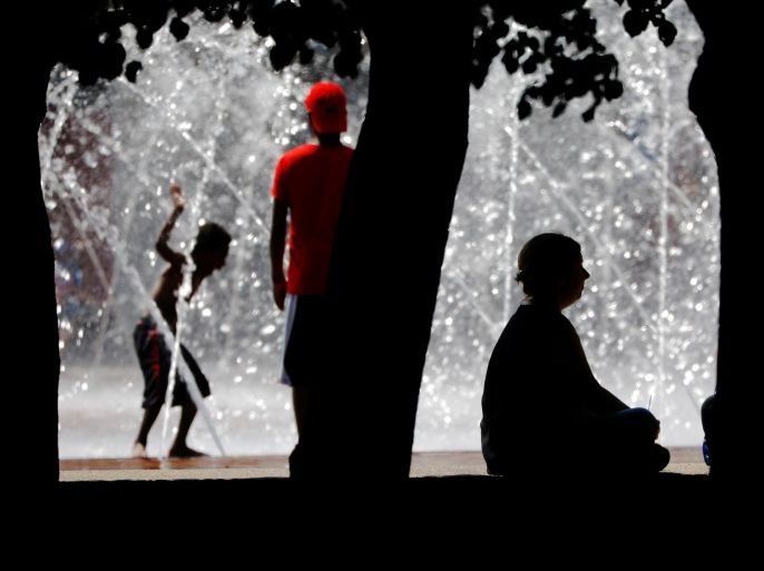 People sit in the shade and cool off in a fountain during a summer heat wave in Boston, Massachusetts, U.S., July 2, 2018. REUTERS/Brian Snyder