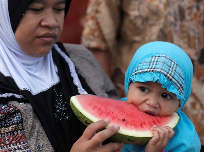 A mother holds her child eating a watermelon during prayers for the Muslim holiday of Eid Al-Adha at Sunda Kelapa port in Jakarta, Indonesia September 1, 2017. REUTERS/Beawiharta