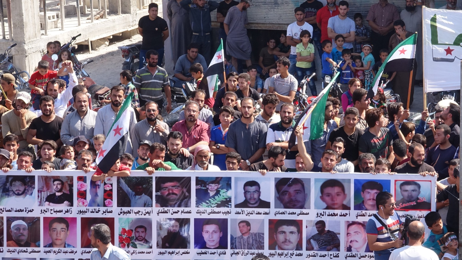 ‪مظاهرة في إدلب ترفع لافتات تضم صور العديد من المعتقلين المغيبين في سجون النظام السوري‬ (الأناضول)