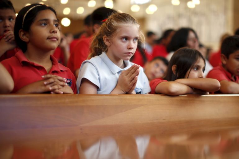 Ruby Park, 11, (2nd L) listens to Pope Francis celebrating the Canonization Mass for Friar Junipero Serra in Washington on a television screen in Los Angeles, California, United States, September 23, 2015. Pope Francis took one of the most controversial steps of his U.S. visit on Wednesday when he canonized an 18th-century missionary known by admirers as the