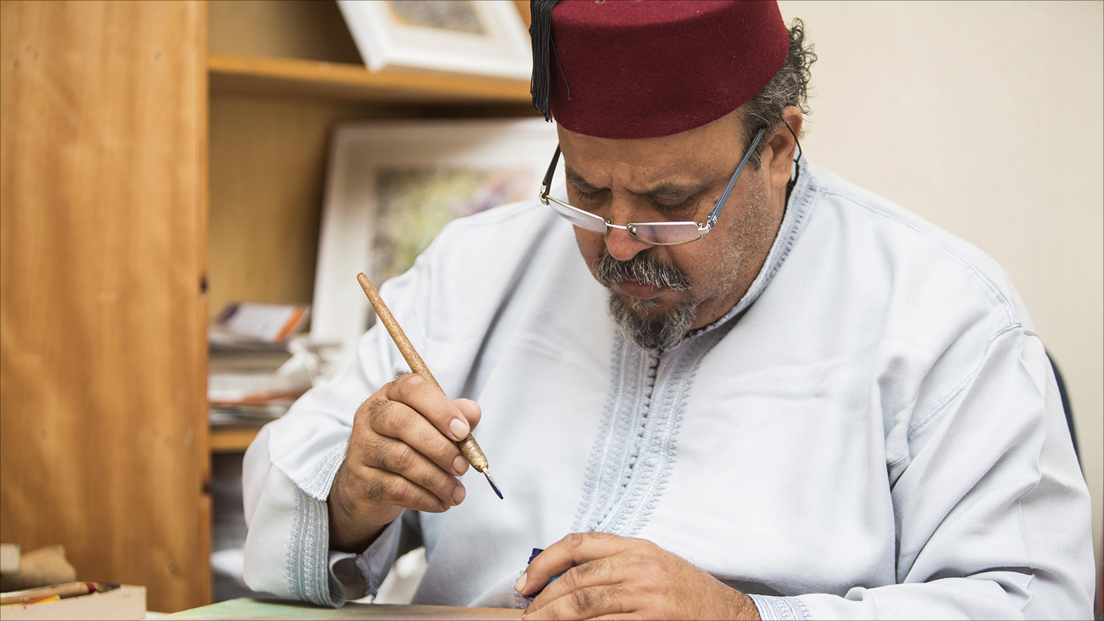 الصانع التقليدي والخطاط عزيز مشاشتي يخط حروفا أبجدية على لوحة فنية (الجزيرة)