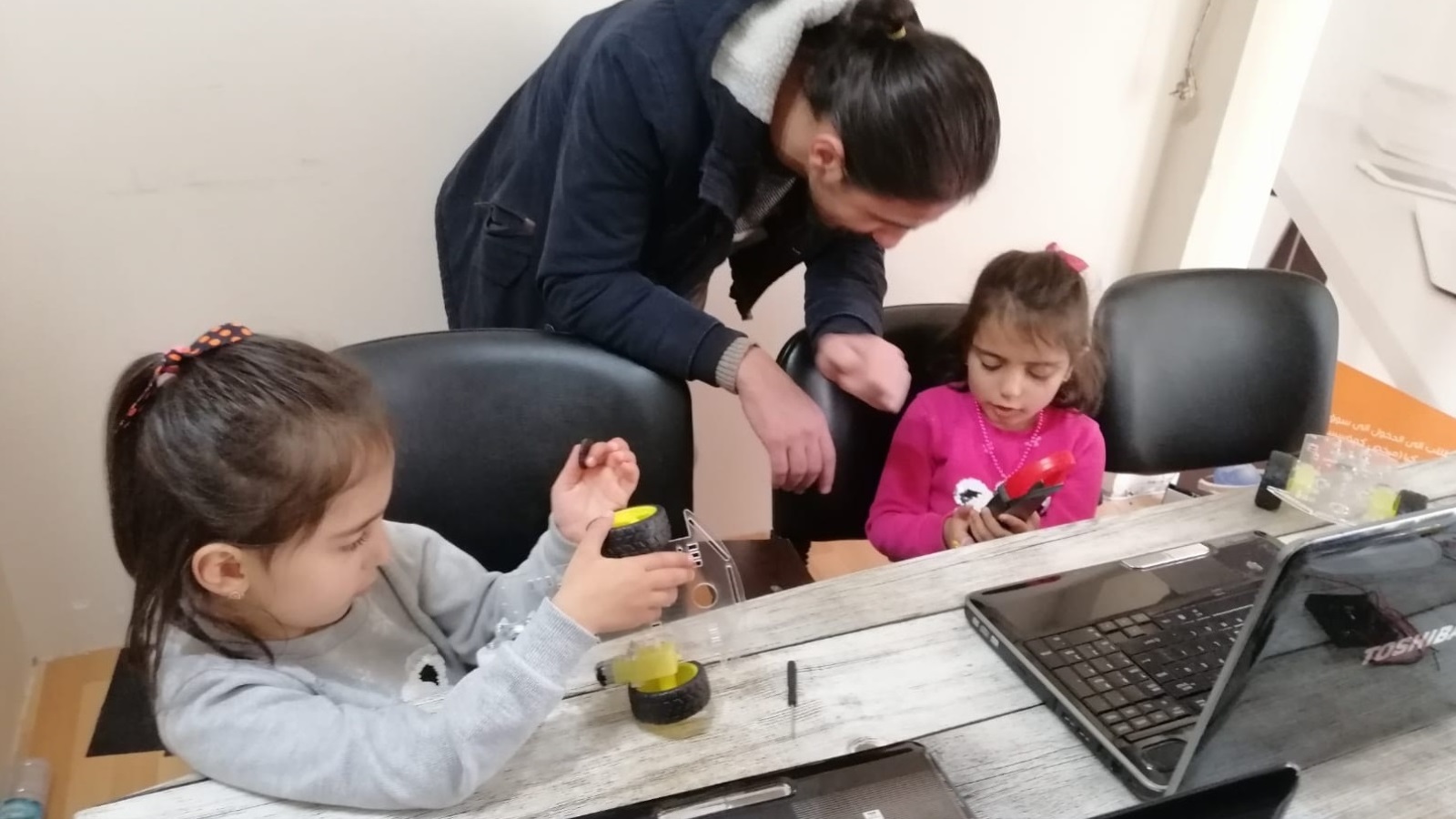 مدرب يساعد طفلتين على تركيب لوح الأردوينو بقطع ألعاب (الجزيرة)