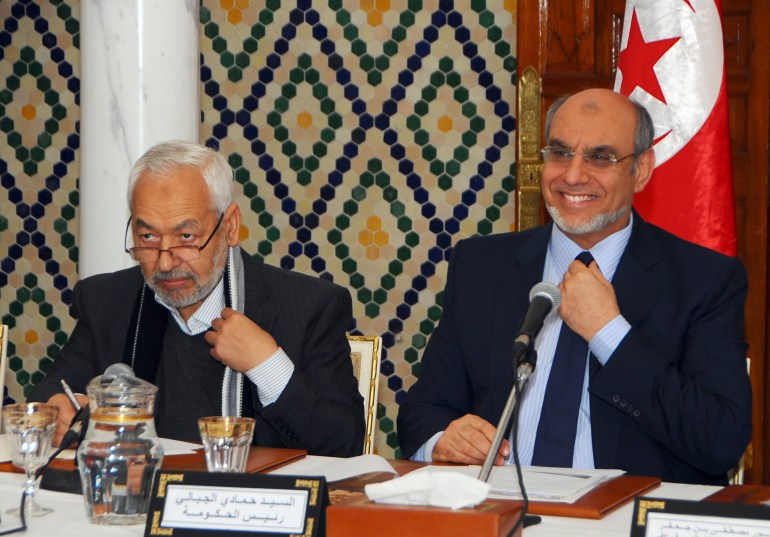 Tunisian Prime Minister Hamadi Jebali, right, smiles at the opening of a meeting with representatives of all Tunisian political parties, to see if there is sufficient support for his solution to end the country's ongoing political crisis in Carthage, outside Tunis, Monday, Feb. 18, 2013. Ennahda party leader Rached El Ghannouchi is seated at left. Jebali's initiative, while supported by the opposition, puts him on a collision course with the moderate Islamist Ennahda Party which dominates the government. (AP Photo/Hassene Dridi)