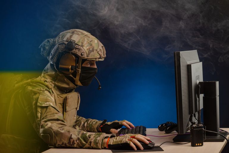 military in uniform sitting at a computer conducts cyber warfare