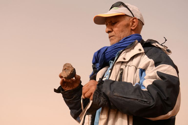 A meteorite hunter examines a rock near the oasis town of Mhamid el-Ghizlane, in southern Morocco's Sahara desert province of Zagora on March 25, 2018. Equipped with a "very strong" magnet and magnifying glass, retired physical education teacher Mohamed Bouzgarine says that discoveries "can be more valuable than gold". (Photo by FADEL SENNA / AFP)v