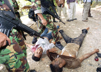 R/Indonesian soldiers stand over the bodies of two slain members of the Free Aceh Movement (GAM) in the village of Loes Kala outside the town of Lhokseumawe on May 25, 2003. The Indonesian Red Cross said on Saturday it had found about 80 bodies in western Aceh province, where a military offensive against rebels began earlier in the week. REUTERS/Supri