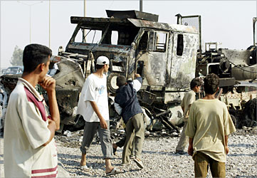 F_An Iraqi boy throws a stone at a burnt out US military transporter carrying other military vehicles in Yussufiyah, 20 kms south of Baghdad, following a rocket propelled grenade (RPG) attack 26 June 2003.