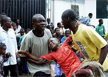 F_Two men carry a wounded boy 21 July 2003 outside the US embassy in Monrovia. At least three people were injured, one of them a US national, in a mortar attack on the US embassy in the Liberian capital Monrovia, the US army command in Europe (EUCOM) said 21 July. "Two mortar rounds fell in and around the embassy," a spokesman, Major Bill Bigelow, told AFP from EUCOM headquarters in Stuttgart. "Reports indicate that there were three injured, one American, I believe a journalist off the compound, and two local contract guards in an annex," Bigelow said. He said that a 41-person US team is providing added security at the embassy. An AFP photographer in Monrovia said the mortar attack, which has not been claimed by either side, seemed to come from the rebel-controlled port area. AFP PHOTO GEORGES GOBET.