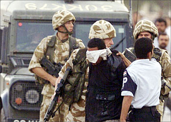 R_British Army soldiers and Iraqi police arrest a man they suspect of planting a roadside bomb in the southern city of Basra November 13, 2003. Grappling with an expanding insurgency, U.S. forces hit back on Wednesday night, destroying a Baghdad warehouse thought to be used by guerrillas and killing two Iraqis in a helicopter strike against a van used to launch mortar attacks on U.S. forces. REUTERS/Atef Hassan