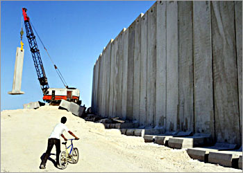 A Palestinian boy pushes a bike next to a wall, a measure Israel contends is necessary to stop suicide bombers and which the Palestinians condemn as a land grab, on the outskits of Jerusalem which will seperate east-Jerusalem neighbourhoods from the West Bank November 20, 2003. Israel responded defiantly on Thursday to unusually sharp criticism by U.S. President George W. Bush of a barrier it is building through Palestinian areas in the West Bank. REUTERS/Reinhard Krause