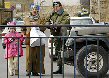 F_A Palestinian woman and her daughter walk next to an Israeli border police in Jerusalem 12 February 2004. Israeli security forces were placed on high alert in readiness for revenge attacks from Hamas as another member of the radical Islamist group was killed, the day after the death of 15 Palestinians in Gaza. AFP PHOTO/Gali TIBBON