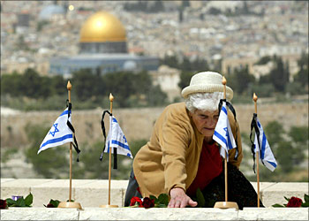 An Israeli woman touches a grave of an Israeli killed during the 1948 war as the Dome of the Rock mosque appears in the background at the military cemetery on the Mount of Olives in Jerusalem during Remembrance Day, which is traditionally marked a day ahead of the anniversary of the creation of the Jewish state, 26 April 2004 in Jerusalem. Israel readied for celebrations marking the 56th anniversary of its creation, which Israelis celebrate as "Independence Day," amid tight security, as a border guard was killed and two others wounded in a southern West Bank Attack.