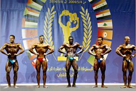 Young arab men perform their routine for the crowd and judges during the finals of the 12th Arab Bodybuilding championship competition in Amman May 7, 2004. REUTERS/Ali Jarekji