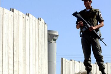 REUTERS - An Israeli border policeman stand in front of the concrete wall part of Israel's controversial security barrier at the check