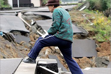 REUTERS - An elderly local resident steps over a gap in the road caused by a powerful earthquake in Nagaoka, northern Japan