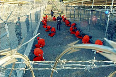 REUTERS/ Detainees in orange jumpsuits sit in a holding area under the watchful eyes of Military Police at Camp X-Ray at Naval Base