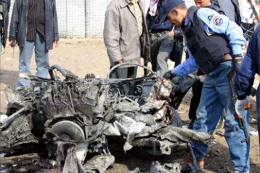 Iraqi policemen inspect what's left of a car bomb outside the Diyala province Police headquarters 07 February 2005