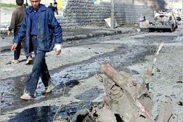 REUTERS /Iraqis walk past the remains of a car bomb after it exploded against a U.S. military convoy in the northern city of Mosul, February 16, 2005. With insurgents still carrying out daily car