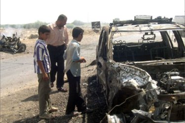 People look at damaged vehicles following a car bomb in the northern city of Samarra 30 August 2005. One policeman was killed and four others wounded when a suicide car bomber blew himself up next to a police checkpoint close to al-Tharthar police station west of Samarra