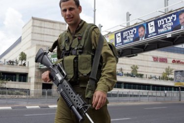 An Israeli soldier patrols 26 March 2006, close to elections posters at a Jerusalem shopping mall. The Israeli security forces are on high alert readying for the Israeli general