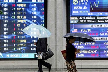 REUTERS/ Pedestrians walk past video screens showing foreign exchange and stock index in Tokyo July 5, 2006. The Nikkei average fell 0.44 percent by midday on Wednesday amid