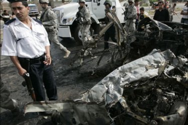 r - An Iraqi policeman (L) and U.S. soldiers secure the scene of a car bomb attack in Baghdad April 26, 2007. At least six people were killed and 15 wounded