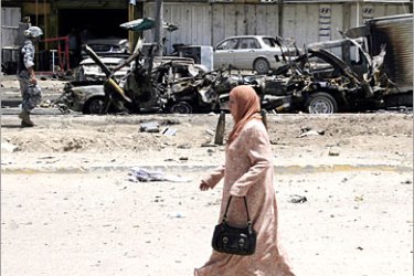 AFP / An Iraqi woman walks past wrecked vehicles at the site of a car bomb in Baghdad's al-Talibiyah neighbourhood, 07 June 2007. Five people were killed and 15 others were wounded