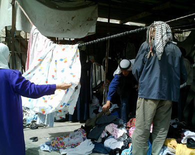 فلسطينيون يقلبون بعض الملابس المستعملة بحثاً عما يصلح لأبنائهم (الجزيرة نت)