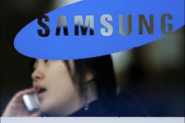 r - A woman uses her mobile phone behind a logo of Samsung Group in Seoul January 31, 2008. A South Korean court ruled on Thursday that Samsung Group companies