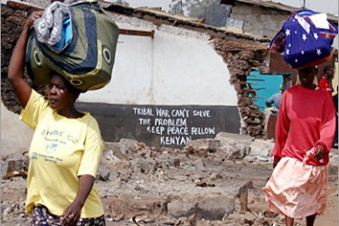 REUTERS/ Internally displaced women carry their belongings as they walk past destroyed houses with graffiti in Nairobi's Kibera slum, February 6, 2008. Kenya's political rivals resumed