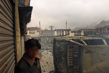 Photo obtained on March 22, 2008 shows a Tibetan man standing by a burnt out vehicle amid clashes