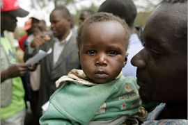 AFP - An internally displaced person (IDP) holds his child while a Kenyan Red Cross worker (L) discusses logistics on June 9, 2008 in Narok, moments after agreeing to leave the IDP camp. Many had sought refuge following fighting that erupted after Raila Odinga, now the prime minister, accused