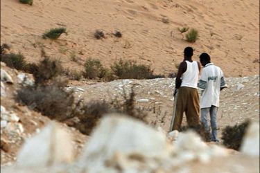 r : Two Nigerian men stand in a border area north of Sinai near Israel as they wait to be smuggled into Israel August 5, 2008. An increasing number of African migrants try to cross