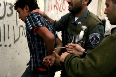 F/Israeli soldiers bind a Palestinian youth's hands during an arrest next to the separation barrier near the West Bank checkpoint of Kalandia, on the outskirts of Ramallah, on September 26, 2008 as Palestinians head towards Jerusalem's Al-Aqsa Mosque for the last Friday prayer of the holy month of Ramadan. Muslims around the world will celebrate on October 1 the Eid Al-Fitr holiday, which marks the end of Islam's holy fasting month of Ramadan. AFP PHOTO/ABBAS MOMANI