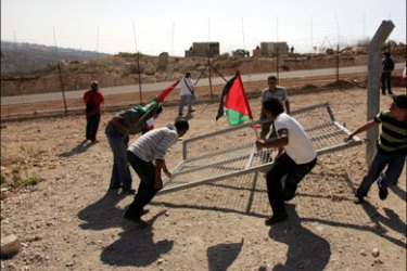 afp ;l Palestinian youths holding national flags remove a fence to be fixed by workers at the spot where Israel's controversial separation barrier passes in the West Bank