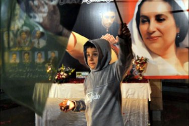 afp : A Pakistani boy holds a flag and a lit earthen lamp on the eve of the first death anniversary of slain former premier Benazir Bhutto in Lahore on December 26, 2008. Tens of