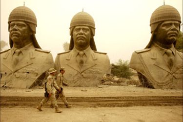f_In the midst of a storm that engulfed the Iraqi capitol, US army soldiers walk past the last remaining statues depicting the ousted dictator of Iraq, Saddam Hussein, at a US camp