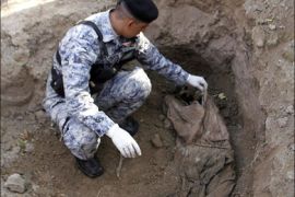 afp : TO GO WITH AFP STORY BY SAMMY KETZ An Iraqi police wearing gloves touches a body in a grave in the orchards close to the Shiite Muslim village of Albu Tumeh in