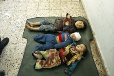 r : A Palestinian man looks at a covered body as the bodies of three children killed by an Israeli tank shell are seen on the floor of the morgue at Shifa hospital in Gaza January 5, 2009.