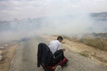A Palestinian protester on a wheelchair is engulfed by teargas fired by Israeli security forces during a protest against the construction of the controversial Israeli