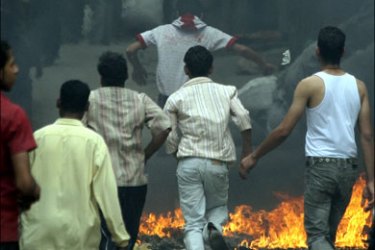 r : People walk through a fire set up by them in the Manshiyat Nasser areas in Cairo, May 3, 2009. Garbage collectors who own pigs clashed with security men who tried to confiscate