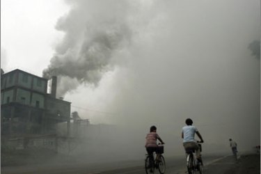 This photo taken on July 18, 2006 shows cyclists passing through thick pollution from a factory in Yutian,