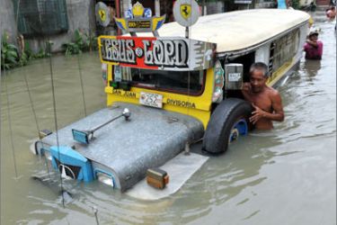 A man pushes a jeepney along a flooded street as residents go along with their daily business in the town of Taytay, Rizal province east of of Manila on October 2, 2009