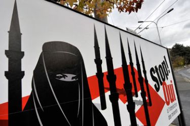 A woman walks behind a campaign posters of the far-right Swiss People's Party depicting a woman wearing a burqa against a background of a Swiss flag upon which several minarets reading in French 'Stop - Yes to the ban on minarets' on November 23, 2009 in Corseaux near Vevey.