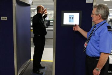 r : A security official (R) prepares to scan his colleague posing inside a RapiScan full-body scanner being trialled by Manchester Airport, during a photocall at the airport, in
