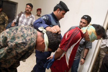 Iraqi policemen escort handcuffed and blindfolded suspect gunmen at a police headquarters in Baghdad on February 22, 1010 after they were arrested in relation to the killing of a family earlier in the day.