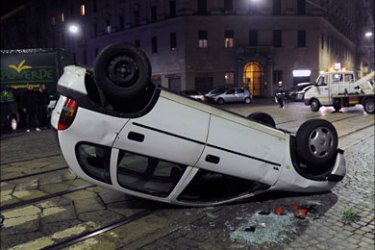 r_An overturned car lies on a street after a riot between North African and South American migrants in downtown Milan February 14, 2010.