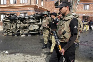 r : Soldiers and police walk past a damaged vehicle at the site of a suicide bomb attack in Mingora, located in Pakistan's restive North West Frontier Province on March 13,