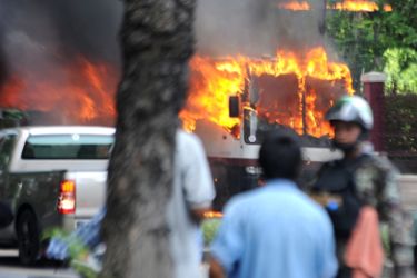 Anti-government protesters stand next to a burning police bus during clashes with Thai soldiers at Lumpini Park in Bangkok on May 14, 2010. Thai troops opened fire